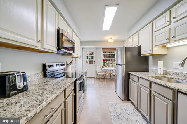 a kitchen with granite countertop a refrigerator a stove a dining table and chairs with wooden floor