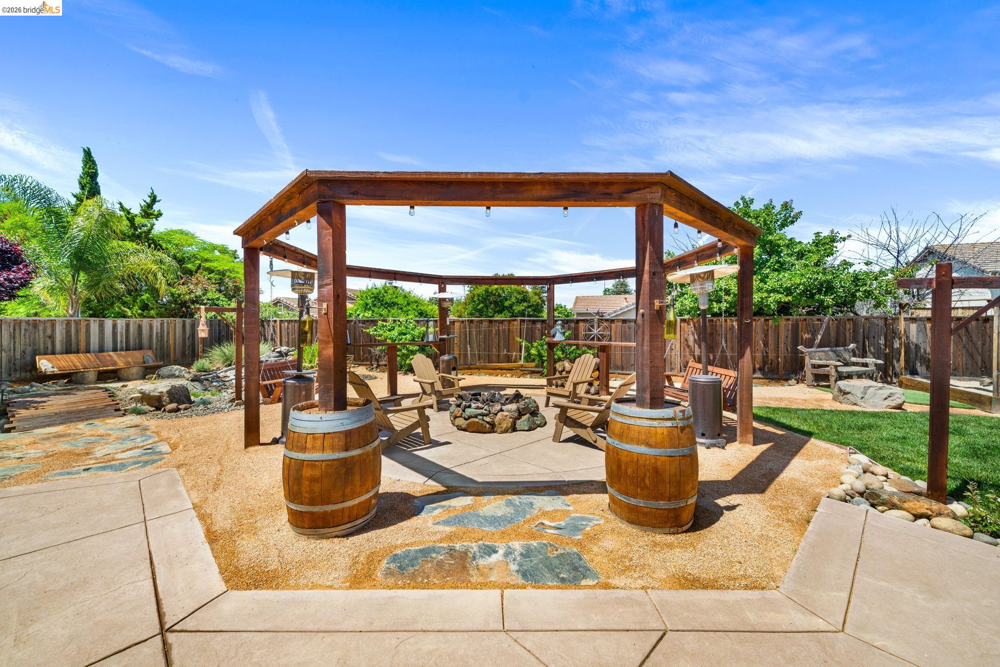 1186 El Rio Court Livermore, CA 94551 - Photo 30 of 60 Expansive outdoor entertaining area featuring a large wooden pergola over a fire pit, surrounded by crushed rock landscaping with natural stone pavers