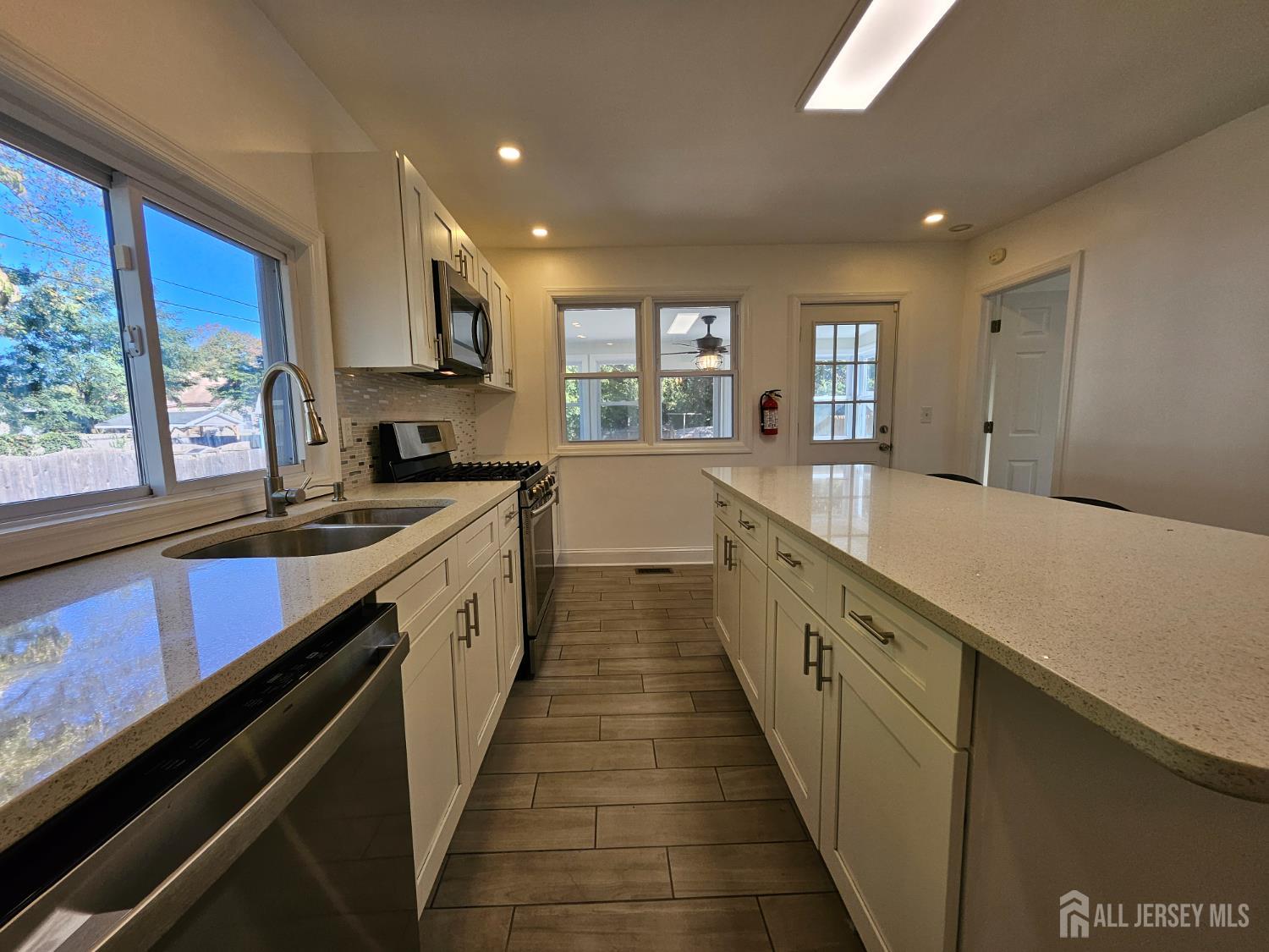 60 6th Avenue Trenton, NJ 08619 - Photo 17 of 28 a large kitchen with stainless steel appliances a sink dishwasher a stove and white cabinets with wooden floor