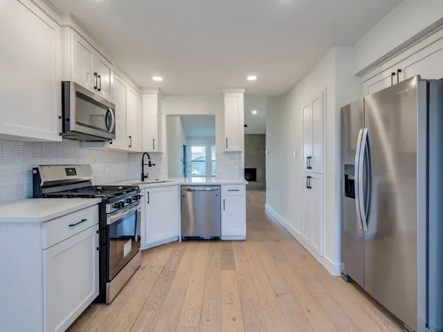 a kitchen with stainless steel appliances granite countertop a refrigerator a stove top oven a sink and dishwasher with wooden floor