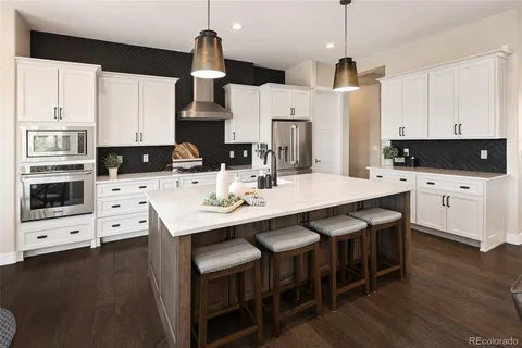 a kitchen with stainless steel appliances a stove a sink a microwave a refrigerator and white cabinets with wooden floor