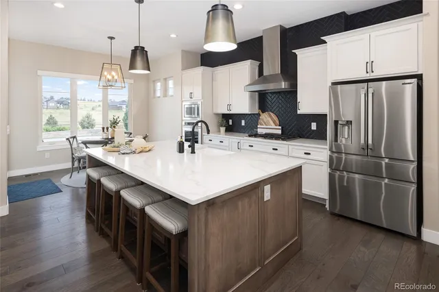 a kitchen with stainless steel appliances a sink a stove a refrigerator cabinets and a dining table with wooden floor