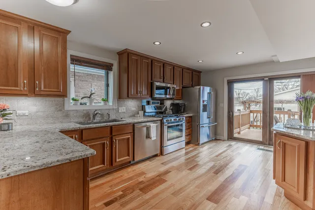 a kitchen with stainless steel appliances granite countertop a stove a sink dishwasher a refrigerator and a microwave oven with wooden floor