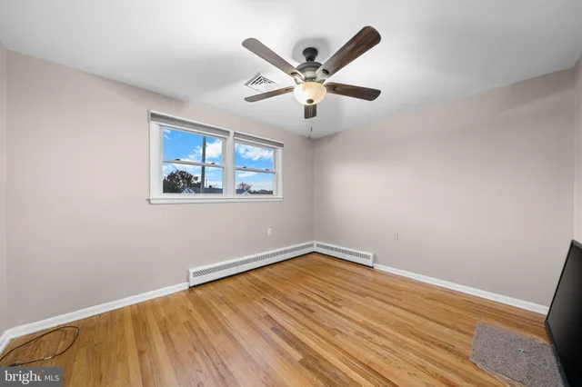 a view of an empty room with wooden floor and a ceiling fan