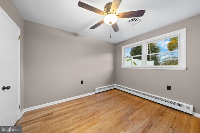 a view of empty room with wooden floor and fan