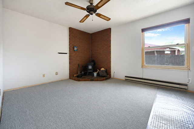 285 West 600 North, Unit 2 Logan, UT 84321 - Photo 3 of 21 Living area featuring a brick-accented corner with a wood-burning stove, gray carpet flooring, and a ceiling fan