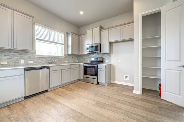 a kitchen with stainless steel appliances granite countertop a stove a sink dishwasher a refrigerator and white cabinets with wooden floor