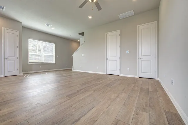 a view of an empty room with wooden floor and a ceiling fan