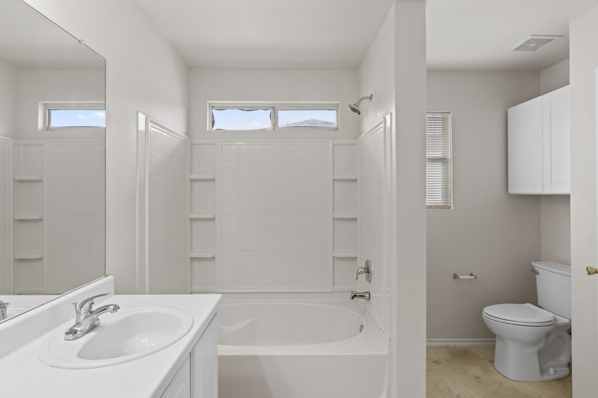 208 Dandelion Loop Kyle, TX 78640 - Photo 25 of 39 Primary bathroom features a vanity with an integrated sink and chrome faucet, a bathtub with a tiled surround, and a separate toilet area with wall-mounted storage cabinets