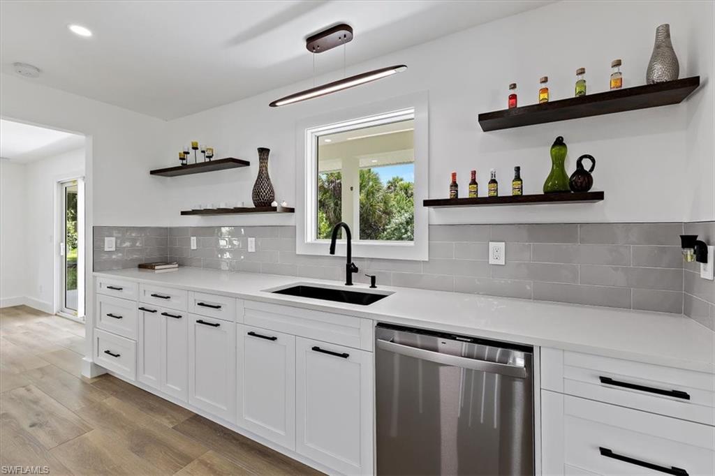 261 13th Street Southwest Naples, FL 34117 - Photo 17 of 35 Kitchen with backsplash, light hardwood / wood-style floors, stainless steel dishwasher, sink, and white cabinets