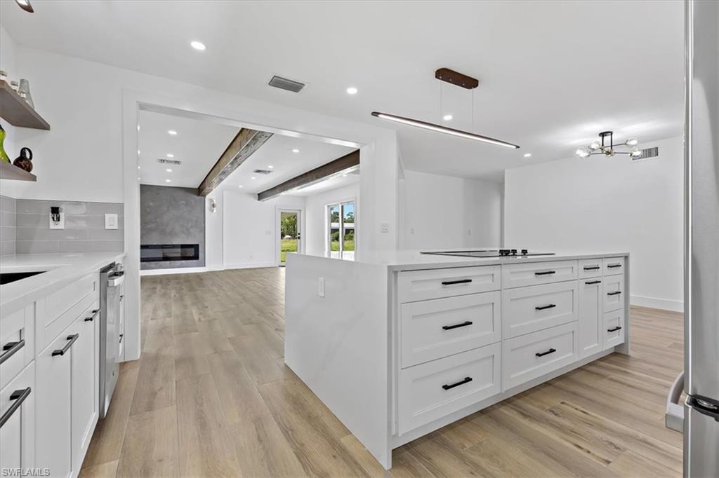 261 13th Street Southwest Naples, FL 34117 - Photo 21 of 35 Kitchen with white cabinets, hanging light fixtures, light hardwood / wood-style flooring, a kitchen island, and stainless steel dishwasher