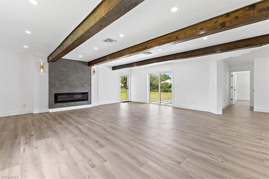 261 13th Street Southwest Naples, FL 34117 - Photo 5 of 35 Unfurnished living room featuring light hardwood / wood-style flooring, beamed ceiling, and a fireplace