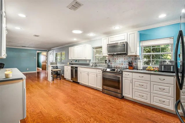 a kitchen with stainless steel appliances granite countertop a stove top oven a sink dishwasher a dining table and chairs with wooden floor