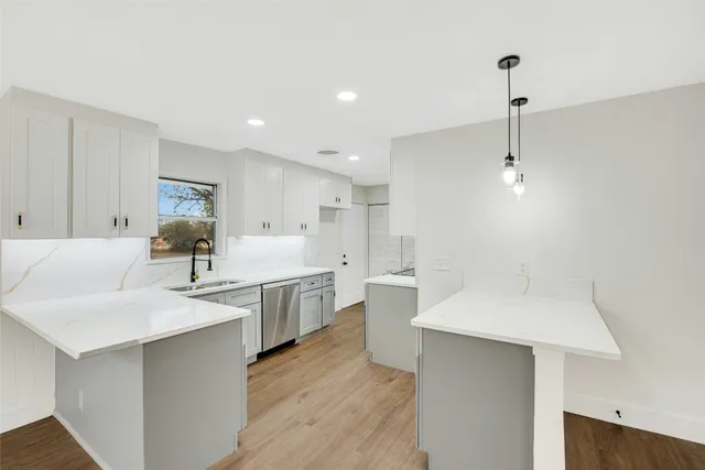 a large white kitchen with a sink and dishwasher a stove with wooden floor