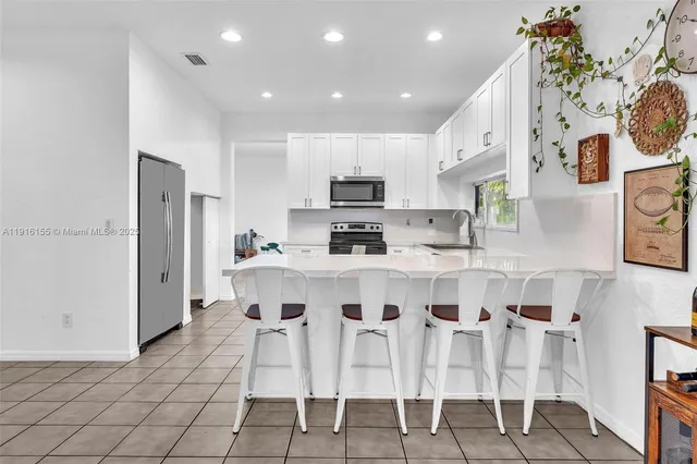 a kitchen with stainless steel appliances kitchen island granite countertop a dining table chairs and a refrigerator