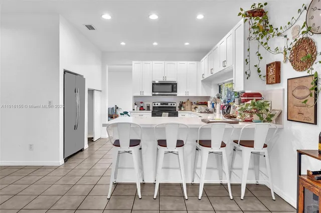 a kitchen with stainless steel appliances kitchen island granite countertop a dining table chairs and a refrigerator