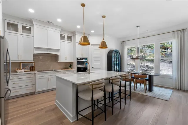 a kitchen with stainless steel appliances granite countertop a stove a sink a oven a dining table and chairs with wooden floor