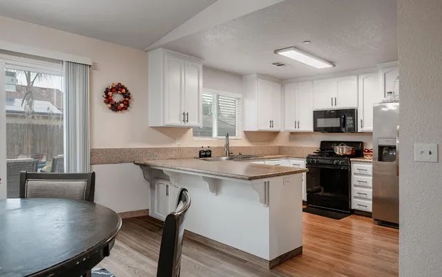 a kitchen with stainless steel appliances granite countertop a stove top oven a sink dishwasher a dining table and chairs with wooden floor