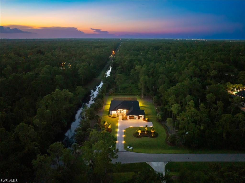 4751 1st Avenue Southwest Naples, FL 34119 - Photo 25 of 25 Spacious property featuring a prominent single-story residence, a long paved driveway, manicured lawns with mature trees, and a bordering waterway