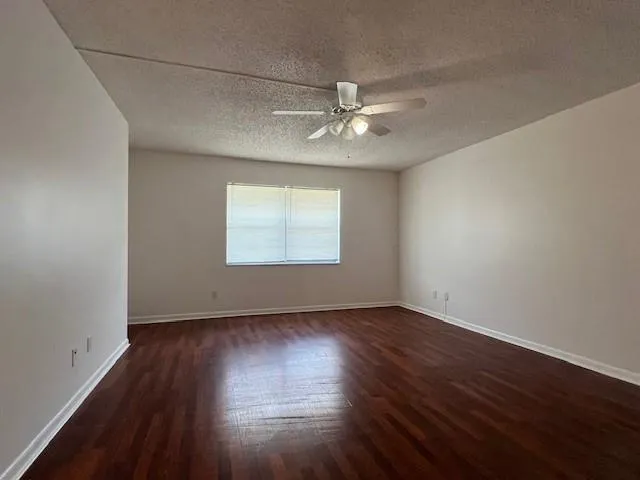 an empty room with wooden floor chandelier fan and windows