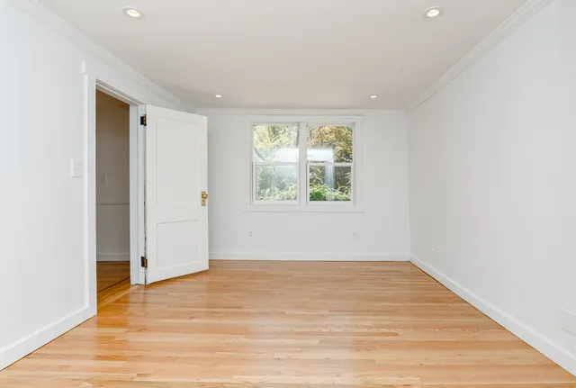 a view of an empty room with wooden floor and a window