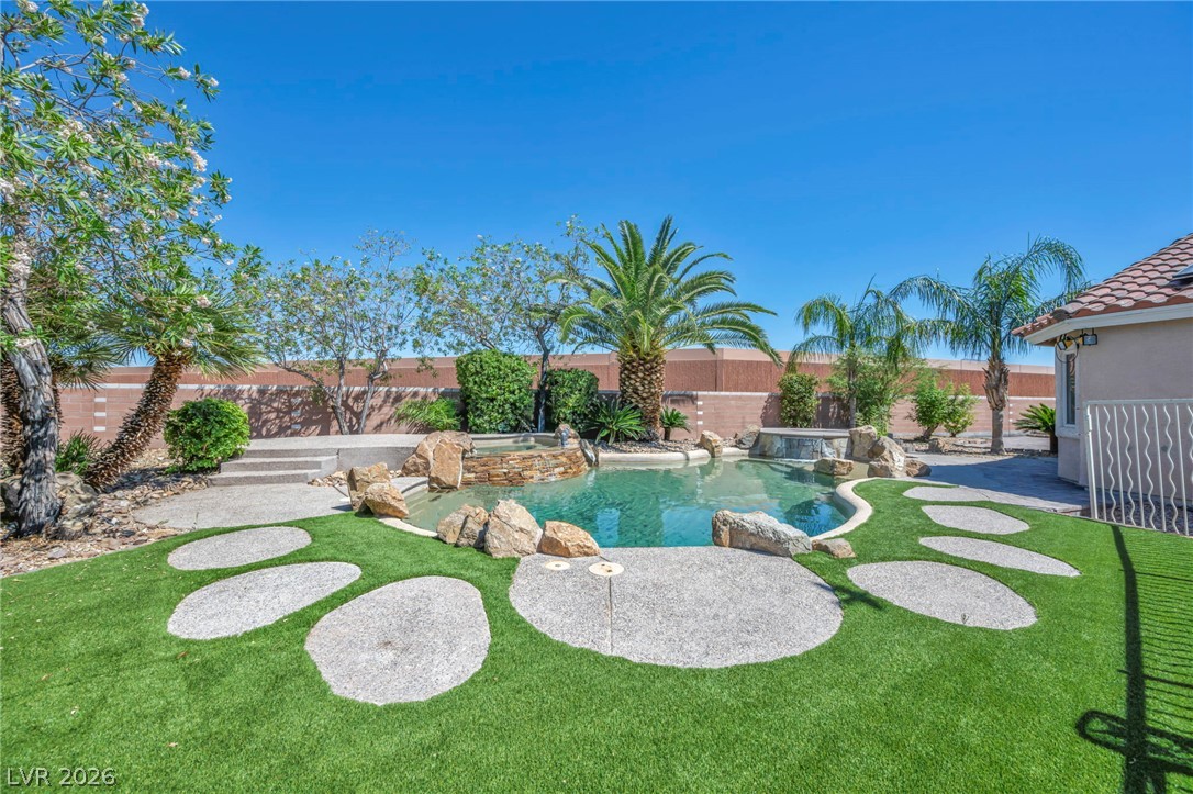 6405 North Raptor Court North Las Vegas, NV 89084 - Photo 44 of 66 A private backyard oasis features an inviting inground pool with rock accents and a spa, set against vibrant green landscaping.