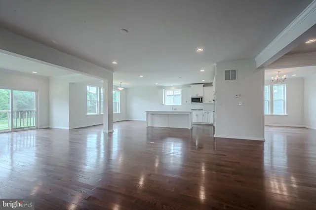 a view of an empty room with wooden floor and a kitchen