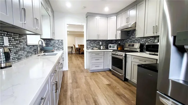 a kitchen with stainless steel appliances granite countertop a stove top oven a sink dishwasher and a refrigerator with wooden floor