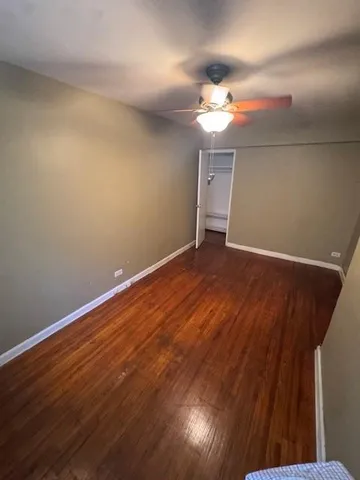a view of an empty room with wooden floor and a ceiling fan