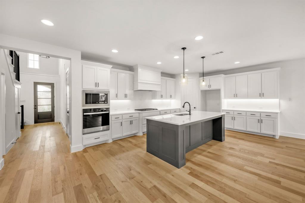 3420 Brocco Road Celina, TX 75009 - Photo 11 of 27 Open-concept kitchen with light wood-finish flooring, white cabinetry, a large kitchen island, and stainless steel built-in appliances