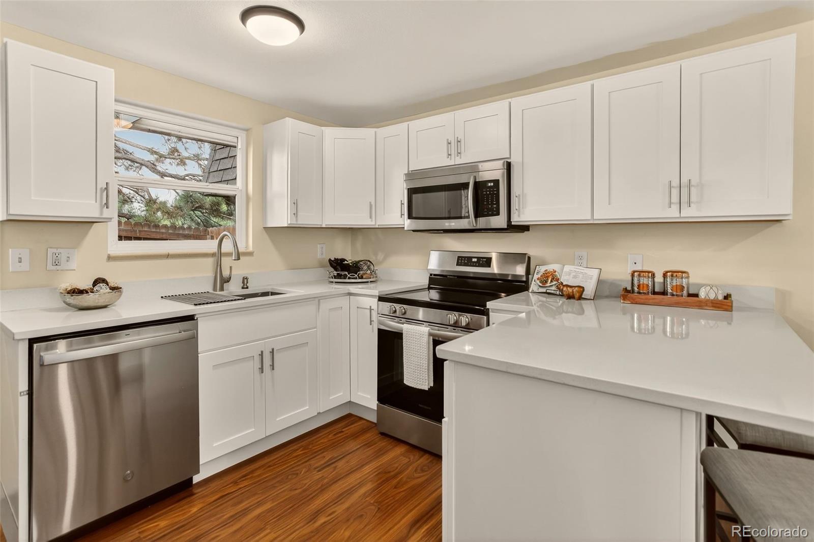 a kitchen with stainless steel appliances granite countertop white cabinets a sink a stove a refrigerator and microwave with wooden floor