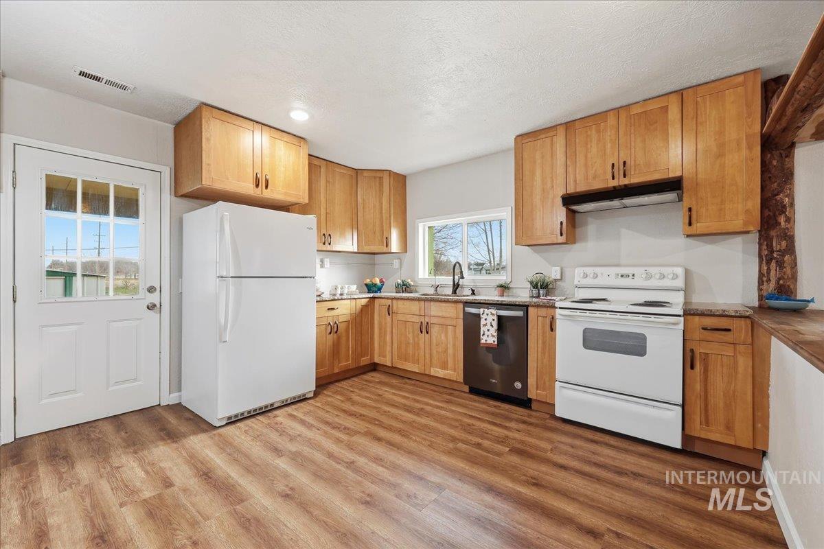 14666 Willis Road Caldwell, ID 83607 - Photo 5 of 23 Kitchen featuring white appliances, under cabinet range hood, light wood-type flooring, light countertops, and a textured ceiling