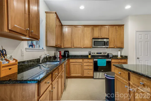 a kitchen with stainless steel appliances granite countertop a stove top oven a sink dishwasher and a microwave with wooden cabinets