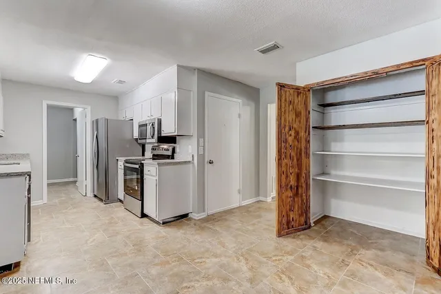 a view of kitchen with refrigerator and white cabinets