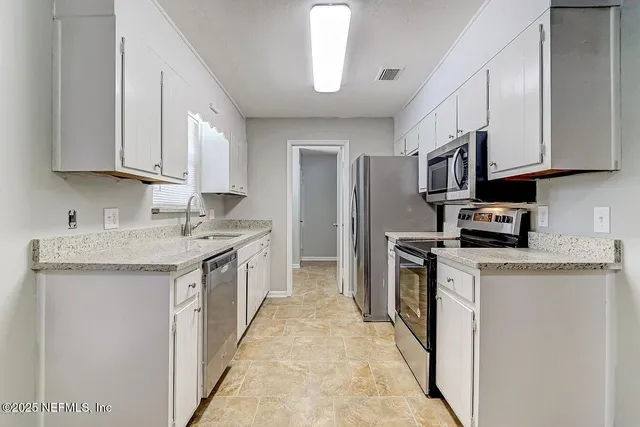 a kitchen with granite countertop a sink a counter top space stainless steel appliances and cabinets