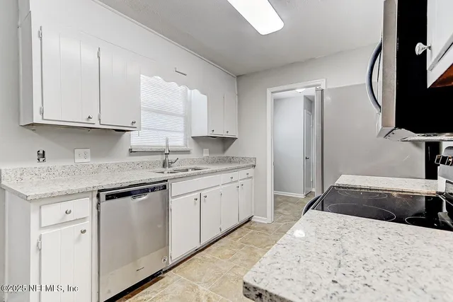 a kitchen with granite countertop a sink stainless steel appliances and white cabinets