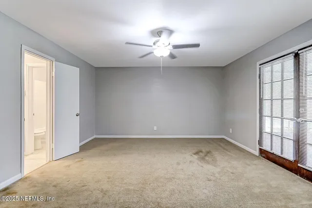 an empty room with chandelier fan and windows