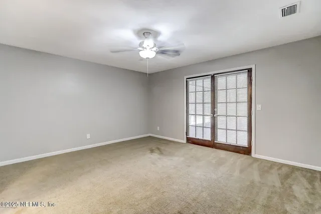 an empty room with chandelier fan and windows