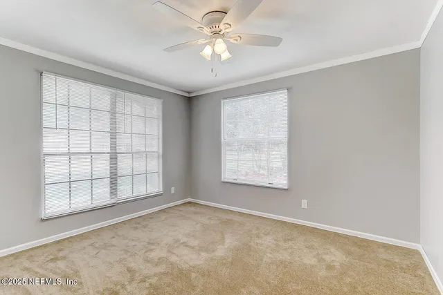 an empty room with chandelier fan and windows