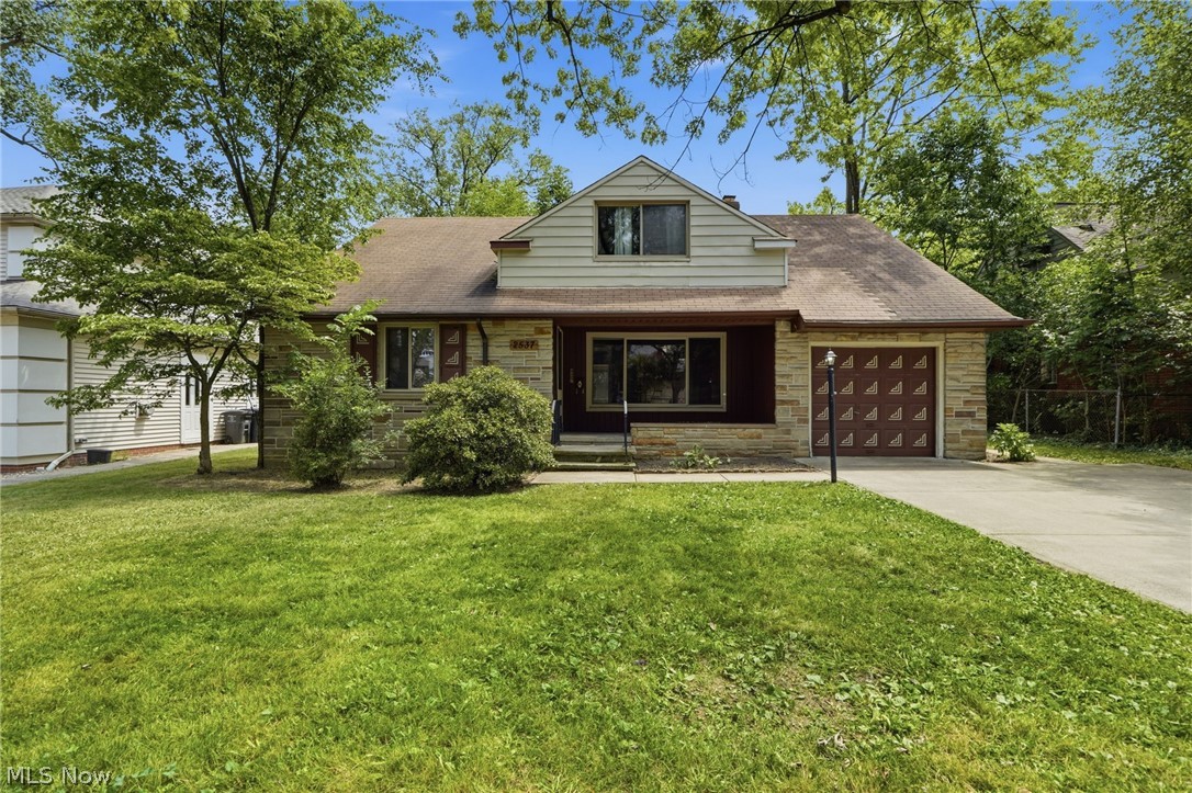 Traditional-style home featuring a prominent front lawn, stone facade accents, an attached garage with a decorative door, and a paved driveway