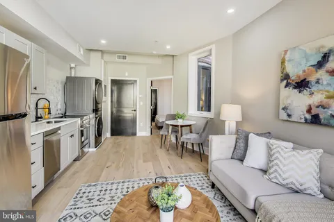 a living room with stainless steel appliances furniture a rug and a kitchen view