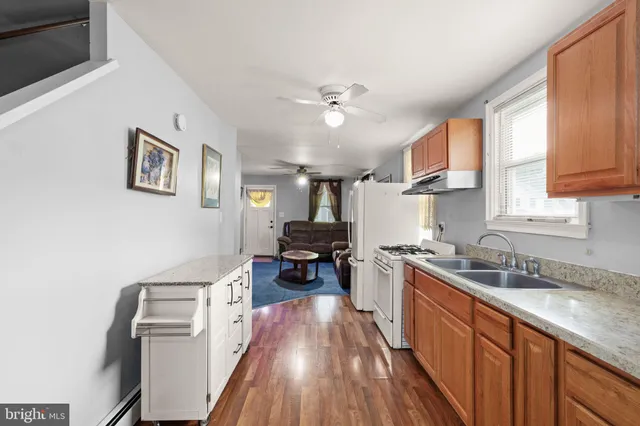 a kitchen with stainless steel appliances granite countertop a refrigerator a sink dishwasher a stove and white countertops with wooden floor