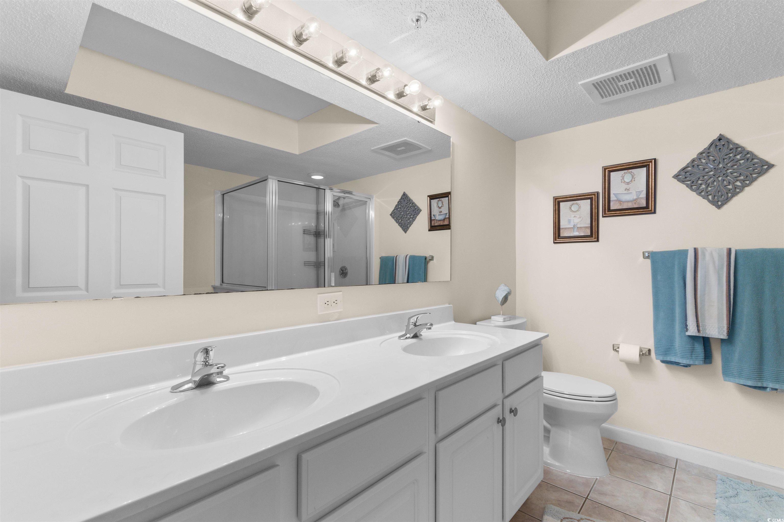 1003 South Ocean Boulevard, Unit 902 North Myrtle Beach, SC 29582 - Photo 19 of 40 Bathroom with a stall shower, double vanity, light tile patterned floors, and a textured ceiling