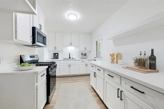 a kitchen with stainless steel appliances a sink stove top oven and white cabinets