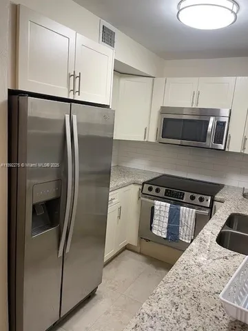 a kitchen with stainless steel appliances granite countertop a refrigerator a stove and a sink with wooden floors