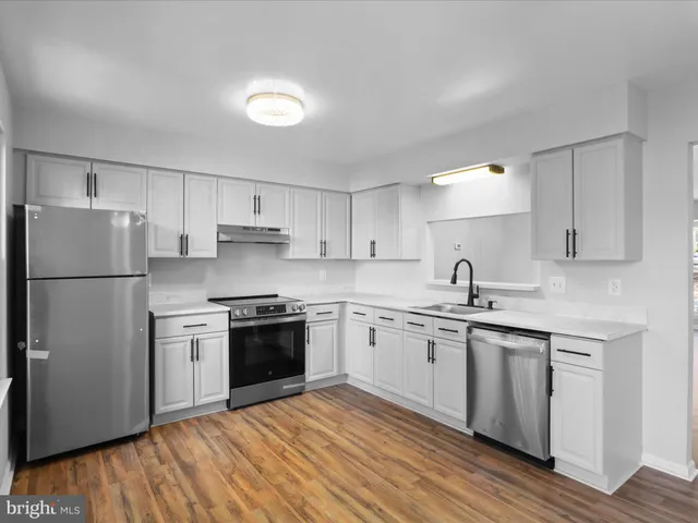 a kitchen with stainless steel appliances granite countertop a stove a sink dishwasher a refrigerator and white cabinets with wooden floor