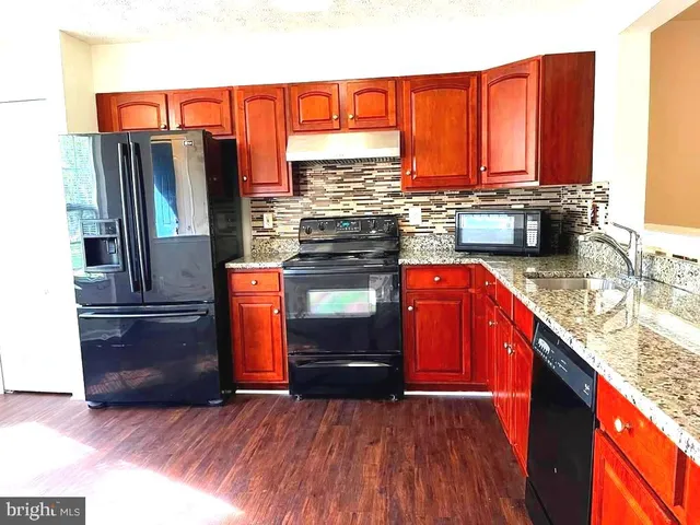 a kitchen with stainless steel appliances granite countertop a refrigerator a sink dishwasher a stove with granite countertops and wooden floor