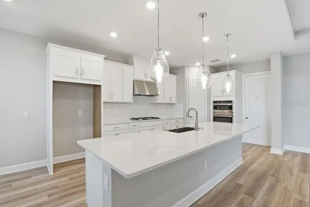 a large kitchen with kitchen island a stove a sink a refrigerator and a wooden floor