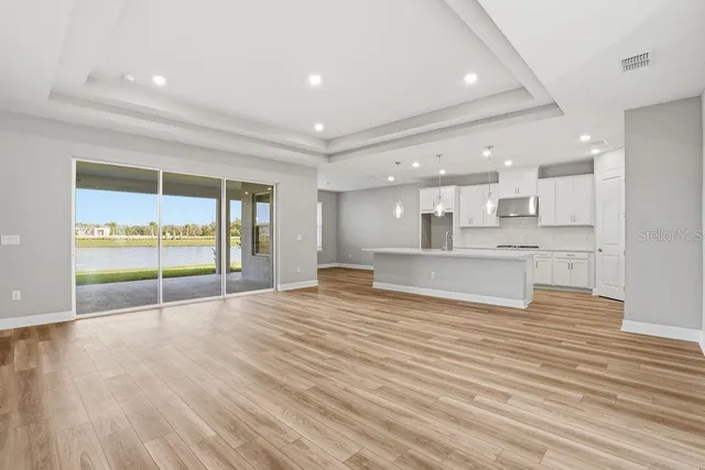 a view of an empty room with wooden floor and a kitchen