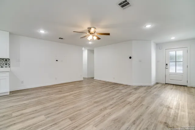 a view of an empty room with wooden floor and a ceiling fan